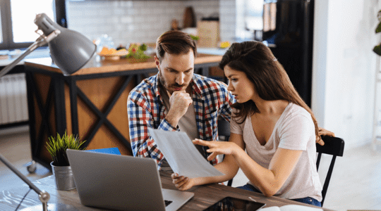 couple looking at paper around computer screen