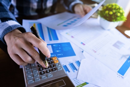 person using calculator with financial papers on desk