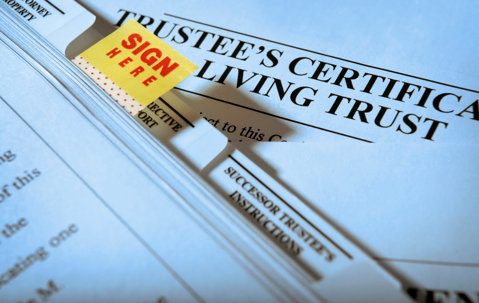 Close-up of living trust paperwork with a “Sign Here” tab beside the trustee’s certificate section.